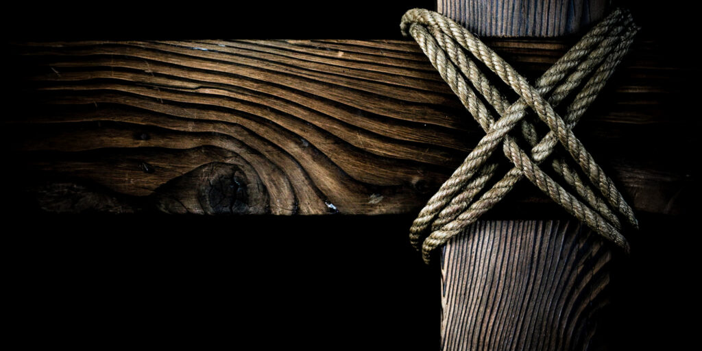 Rope wrapped around middle of cross with dark background.