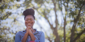 Woman folding her hands in prayer and smiling with blurred trees behind her