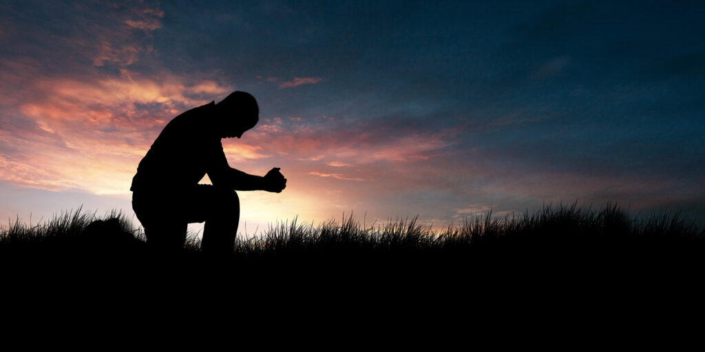 Silhouette of man kneeling to pray